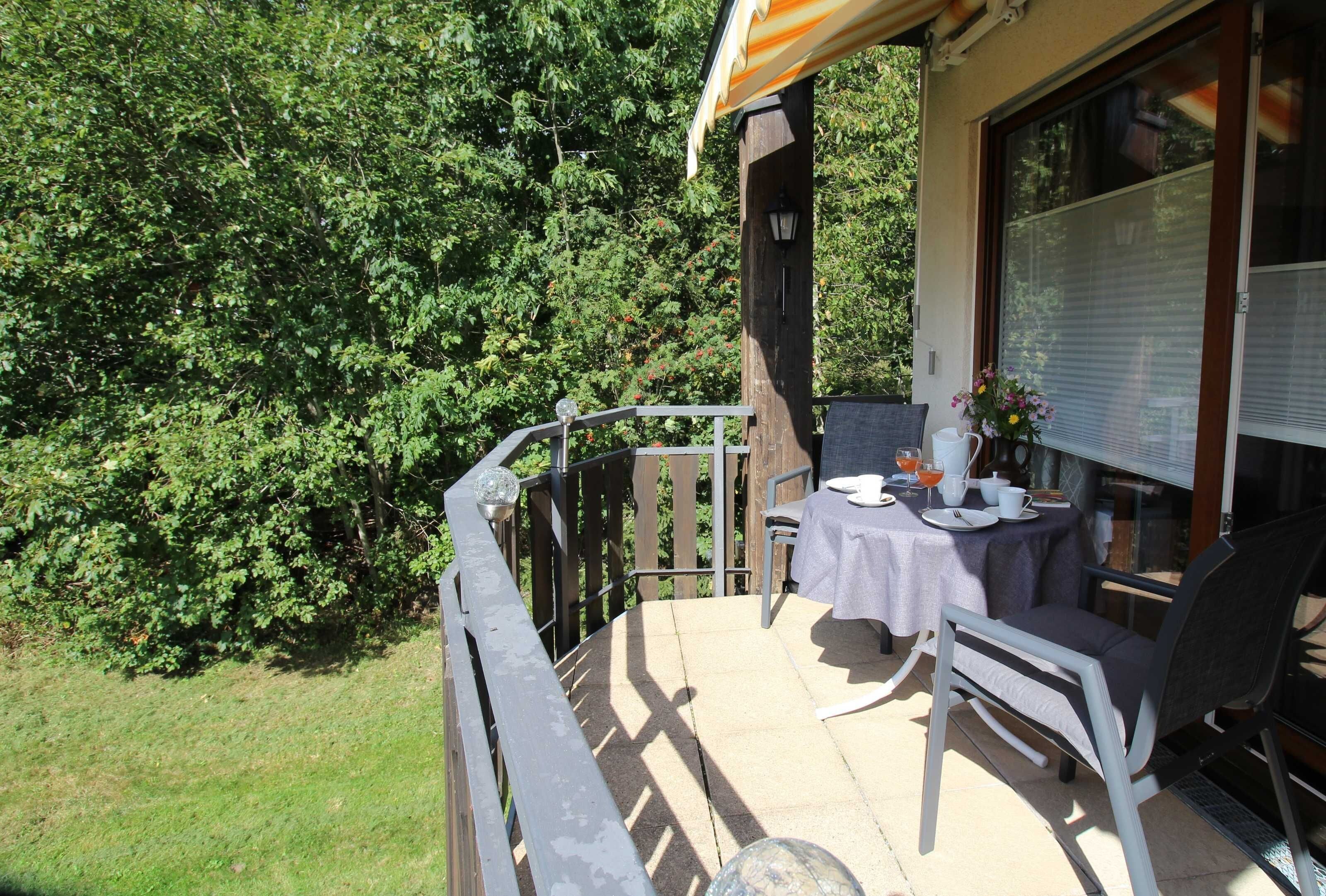 A balcony with a table and chairs, surrounded by greenery.
