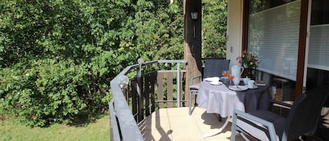 A balcony with a table and chairs, surrounded by greenery.