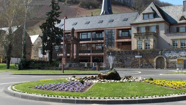 A hotel with a stone facade, multiple windows, and a landscaped garden with flowers.