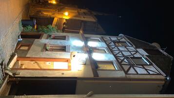 Ein traditionelles Fachwerkhäuschen mit Eingang im Erdgeschoss, einer Treppe, die zu den oberen Stockwerken führt, und einem beleuchteten Fenster, das auf einen Raum im Inneren hinweist.