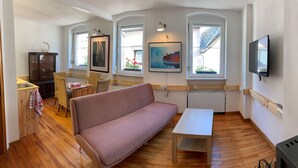 A cozy room with a sofa, a small table, a cabinet with glass doors, and a TV mounted on the wall.