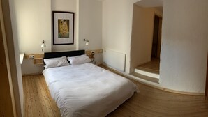 A bedroom with a bed, bedside lamps, a framed artwork, and a wooden floor.
