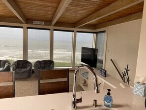 A beach house interior with a large window overlooking the ocean, a television, and a sink with a soap dispenser. - Forever ocean views! Close to one of the cleanest rivers in the world & Redwoods (Smith River)