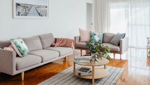 A modern living room with a grey sofa, a round coffee table, and a large window with sheer curtains. - Anchor in Avoca Beach - enjoy your 4 bedroom coastal getaway (Avoca Beach)