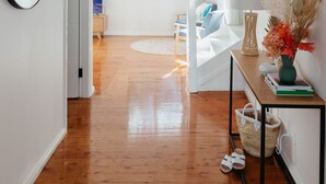 A spacious hallway with wooden flooring, a round mirror, a wicker pendant light, a console table with decorative items, and a staircase leading to another room. - Anchor in Avoca Beach - enjoy your 4 bedroom coastal getaway (Avoca Beach)