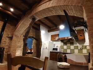 A rustic kitchen with exposed brick walls, wooden beams, a hanging light fixture, a microwave, and a sink. - Albaga - A Rural Loft for Couples   (Sant Jordi)