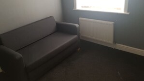 A room with a grey sofa, a radiator, and a window with a view of the outside. - Gateshead's Amethyst 3 Bedroom Apt, Sleeps 6 Guest (Chester-le-Street)