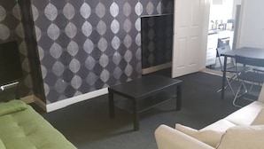 A living room with a patterned wallpaper, a black coffee table, a green sofa, and a white armchair. - Gateshead's Amethyst 3 Bedroom Apt, Sleeps 6 Guest (Chester-le-Street)