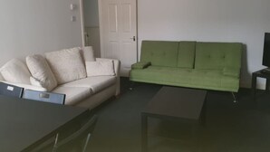 A living room with a beige sofa, a green sofa, a coffee table, and a TV stand. - Gateshead's Amethyst 3 Bedroom Apt, Sleeps 6 Guest (Chester-le-Street)