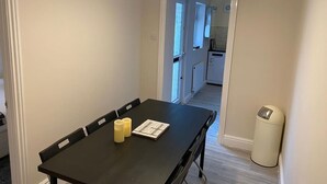 Un coin repas avec une table, des chaises et des bougies. On y trouve également une poubelle et une porte qui donne sur une autre pièce.
