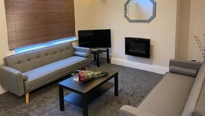 Un salon moderne avec un canapé gris, une table basse noire, un téléviseur à écran plat et une cheminée.