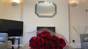 Un salon au design moderne, doté d’un téléviseur à écran plat, d’une table basse en verre ornée d’un bouquet de roses rouges et d’une décoration murale aux motifs géométriques.