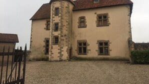 Ein historisches Gebäude mit einem markanten Turm, zahlreichen Fenstern und einem Schotterhof.