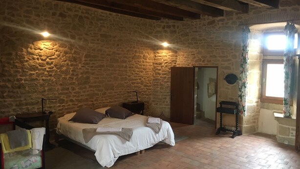 Ein Schlafzimmer mit einer Steinwand, einem Bett mit Kissen, einem Nachttisch, einem Holzschrank und einem Fenster mit Vorhängen.
