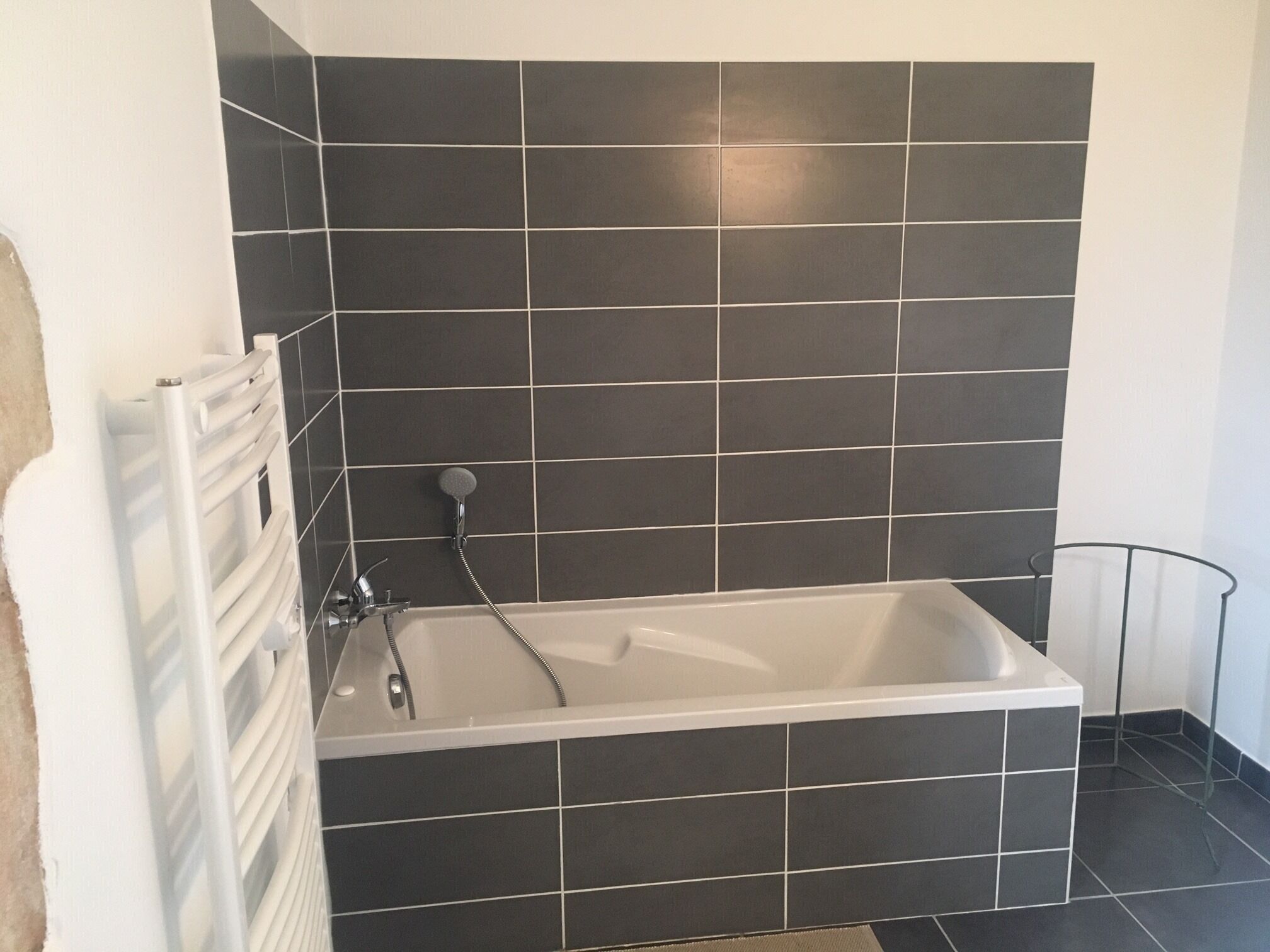 A modern bathroom with a freestanding bathtub, a white radiator, and dark tiled walls.