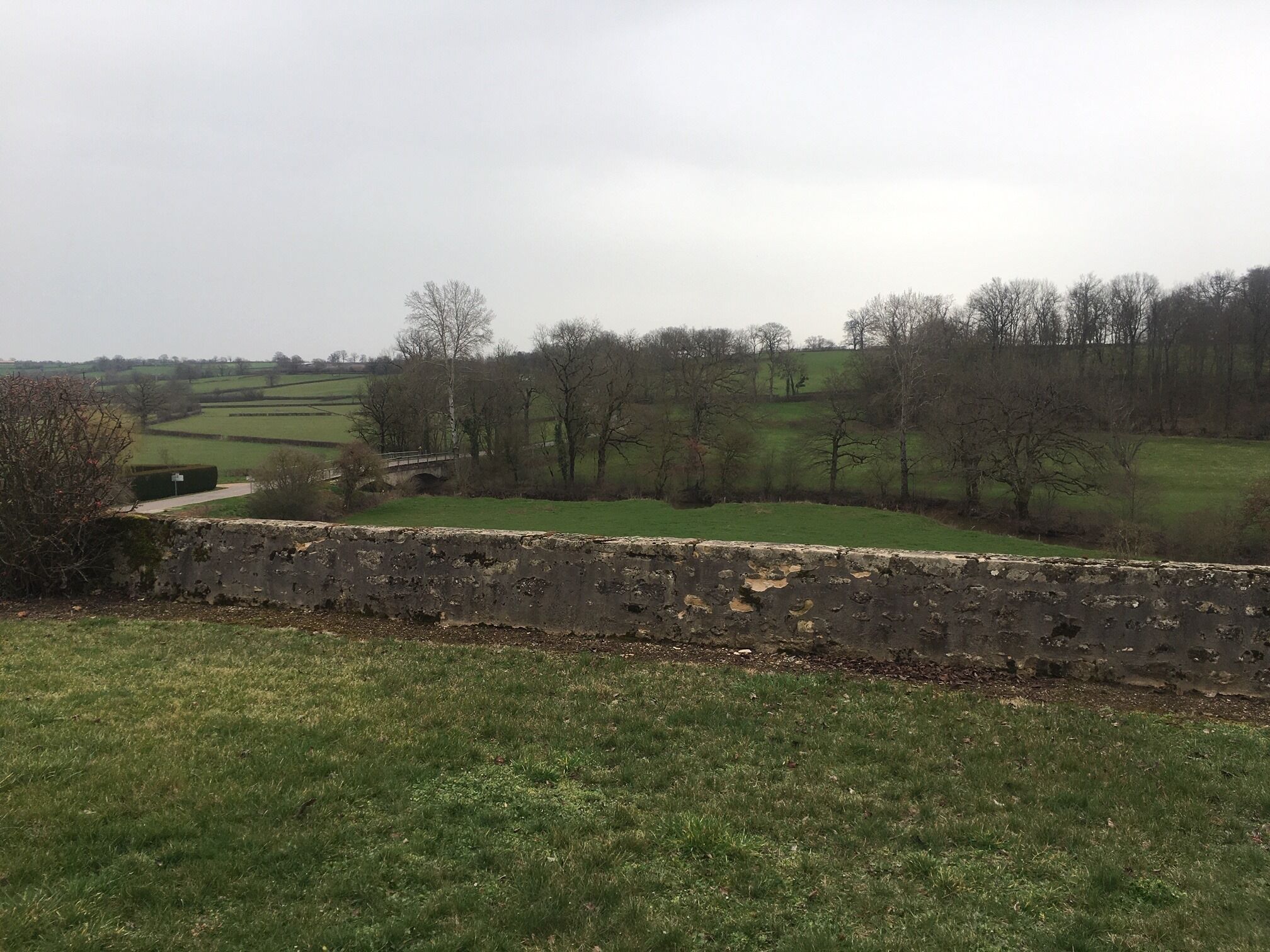 Un mur de pierres, avec un champ herbeux et des arbres en arrière-plan.