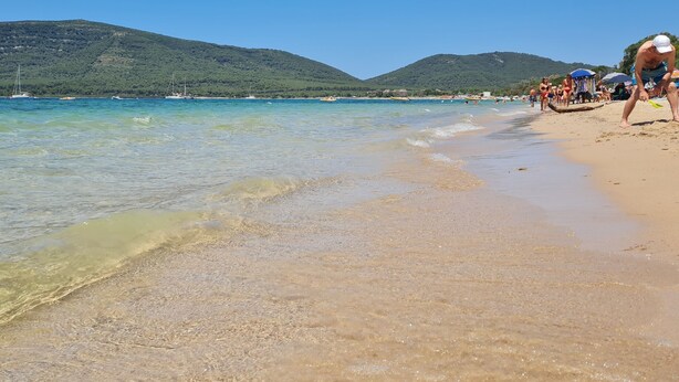 A beach with clear water, a sandy shore, and boats in the distance.