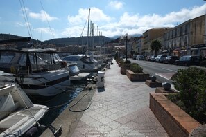A marina with boats docked along a tiled walkway, surrounded by buildings and a road.