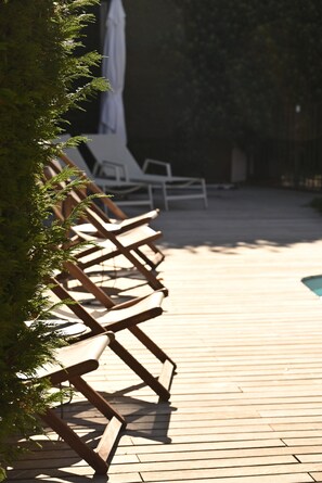 Una terraza de madera con sillones de descanso y una piscina.