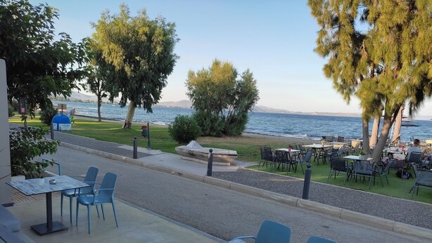 Un espace extérieur aménagé avec des tables et des chaises, offrant une vue sur une étendue d’eau et une chaîne de montagnes lointaine.
