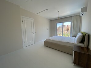 A bedroom with a large bed, a window with a view of buildings, a door, and an air conditioning unit. - Petrum Sunset (Bodrum)