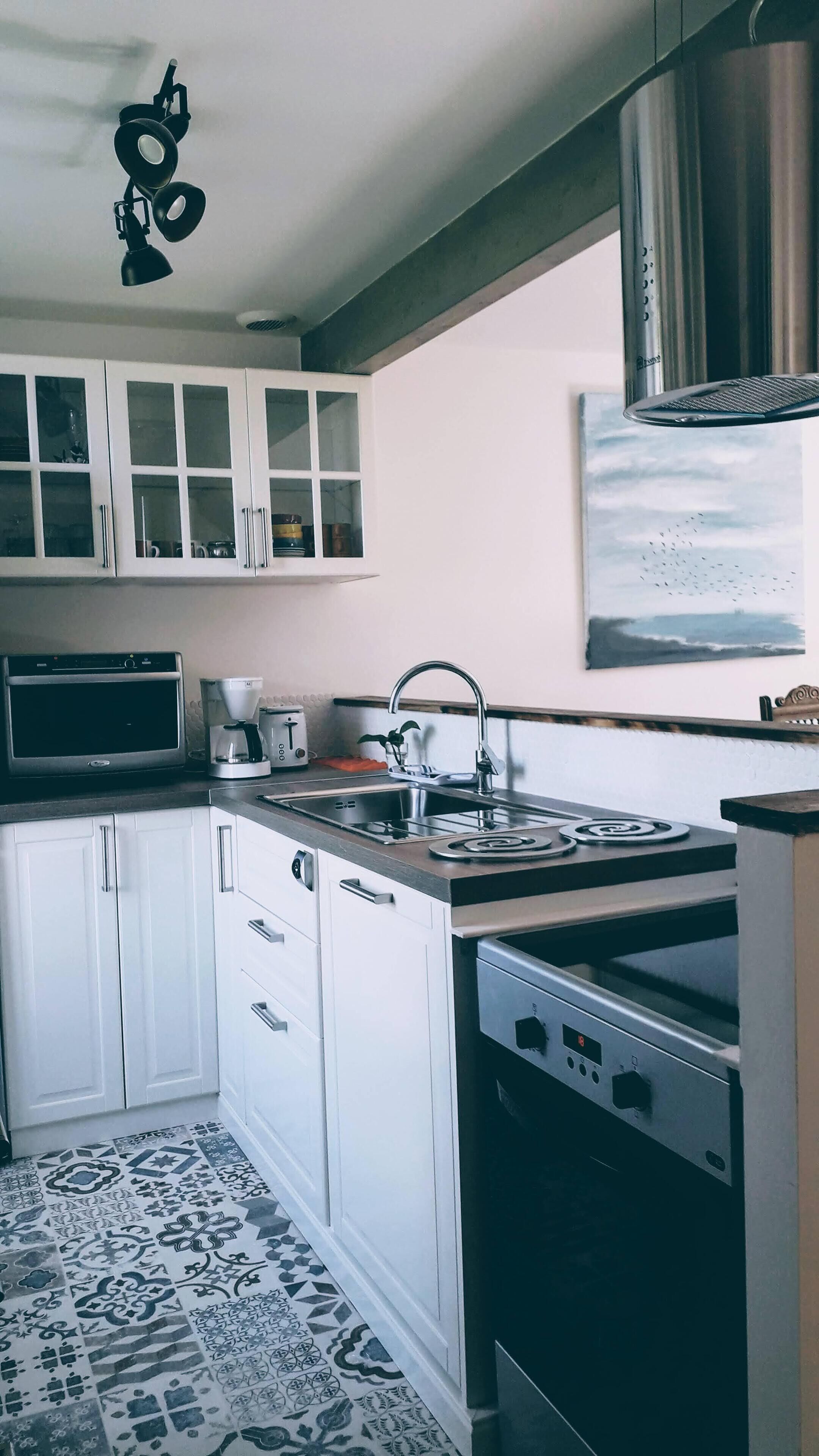 A modern kitchen with white cabinets, a stainless steel sink, a stove, and a coffee maker.