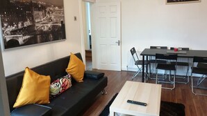 A living room with a black sofa, yellow cushions, a coffee table, and a dining area with a table and chairs. - South Shield's Hidden Gem Garnet 3 Bedroom Apartme (South Shields)