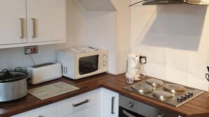 A compact kitchen with white cabinets, a microwave, a toaster, a slow cooker, a coffee maker, and a stove. - South Shield's Hidden Gem Garnet 3 Bedroom Apartme (South Shields)