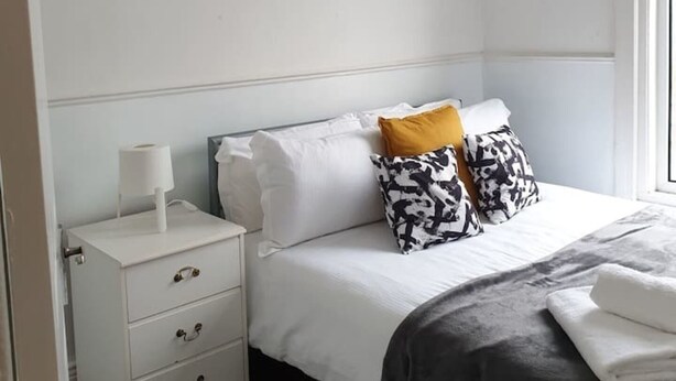 A bedroom with a bed, white nightstand, and a picture of a bridge. - South Shield's Hidden Gem Garnet 3 Bedroom Apartme (South Shields)