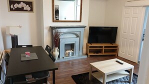 A living room with a fireplace, a TV, a dining table with chairs, and a small coffee table. - South Shield's Hidden Gem Garnet 3 Bedroom Apartme (South Shields)