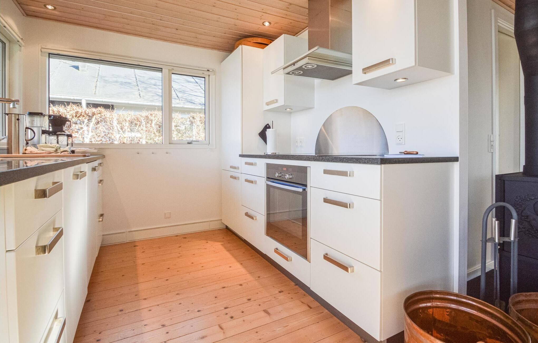 A modern kitchen with white cabinets, a built-in oven, and a large window.
