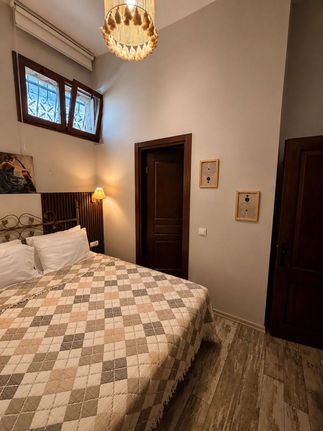 Un dormitorio con una cama, una puerta de madera, una lámpara fijada a la pared y una luminaria en el techo.