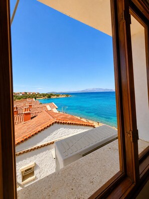 Vista desde una ventana con vista al litoral, tejados de terracota y un mar azul cristalino.