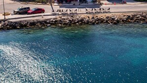 Un hôtel situé sur la côte, avec un bâtiment blanc imposant, un rivage rocheux et une eau d’un bleu limpide.