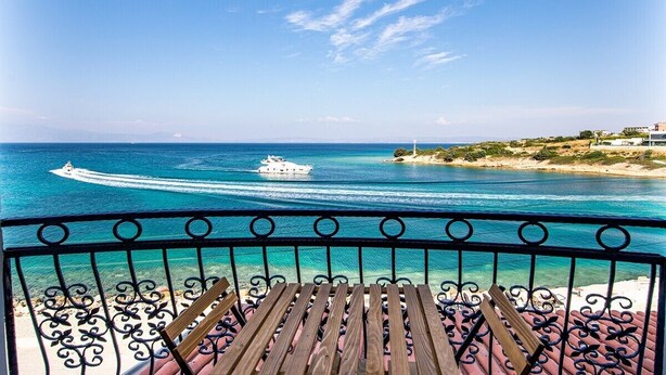 Un balcon avec vue sur la mer, un bateau et une côte lointaine.