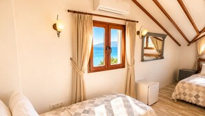 Une chambre avec un plafond en bois, une fenêtre avec des rideaux, un lit recouvert d’une couverture à carreaux, une table de chevet et une petite lampe de chevet.
