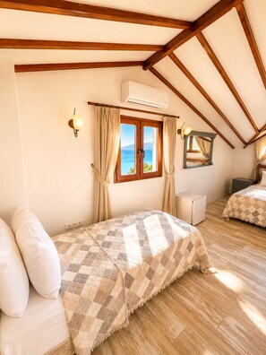 Un dormitorio con techo de madera, una ventana con cortinas, una cama con manta a cuadros, una mesita de noche y una lámpara de noche pequeña.