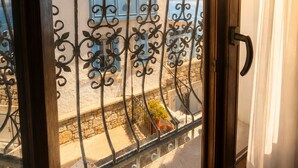 Un balcon orné d’une balustrade en fer forgé, un mur en pierre et, au fond, un bâtiment avec des volets bleus.
