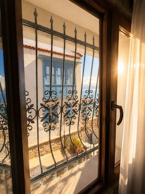 A balcony with a wrought iron railing, a stone wall, and a building with blue shutters in the background. - Mai S'ema Otel Dalyan (Cesme)