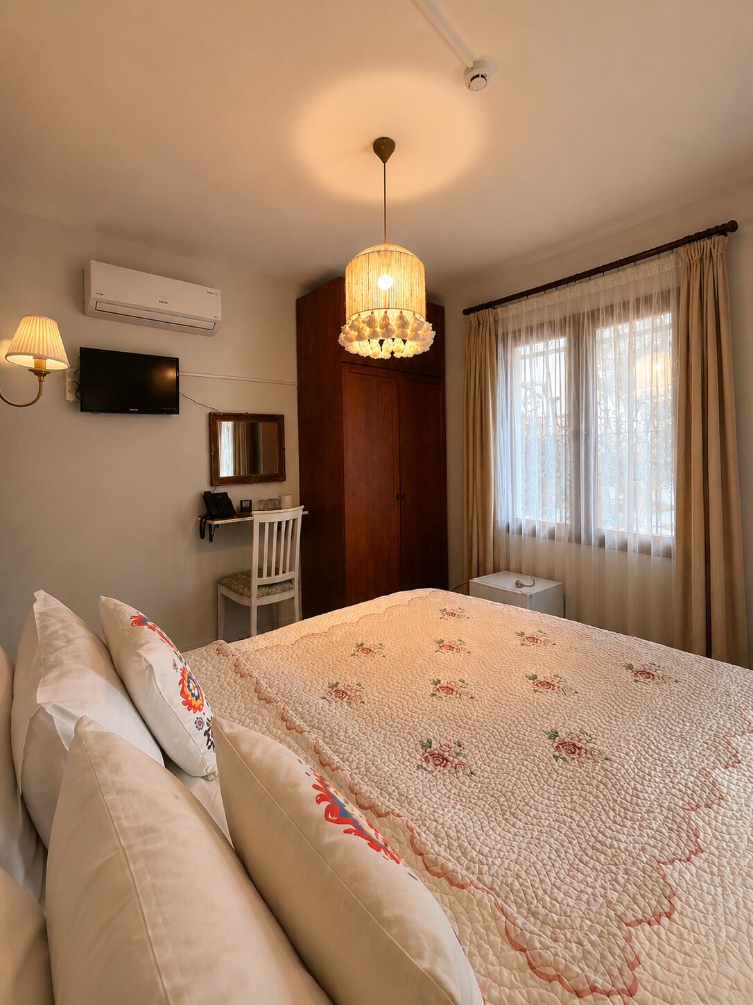 Un dormitorio con cama, escritorio, silla, televisor y ventana con cortinas.