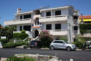 Ein zweistöckiges Gebäude mit Balkon und Treppe, davor ein geparktes Auto.