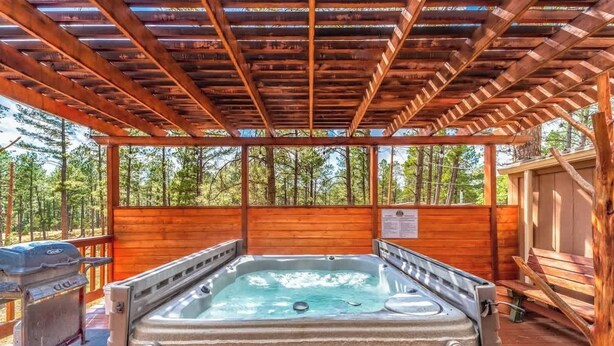 A hot tub under a wooden pergola with a view of trees.