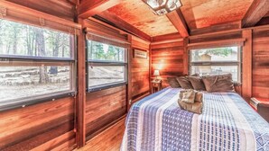 A log cabin bedroom with a bed, windows, and a ceiling light fixture.