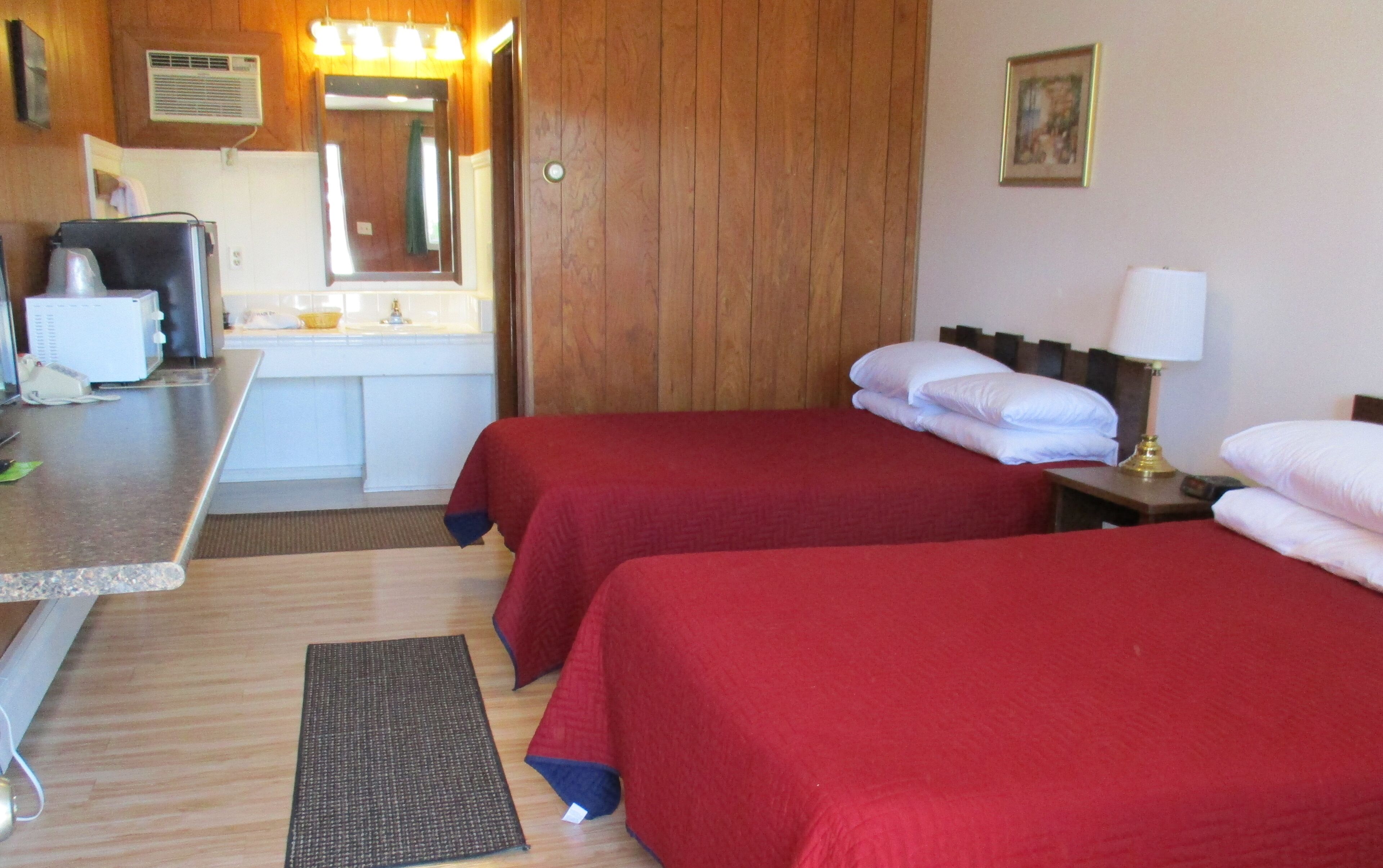 A hotel room with two beds, a desk with a computer, a sink, and a mirror.