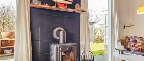 A cozy room with a wood-burning stove, a small sailboat model, and a window with curtains.
