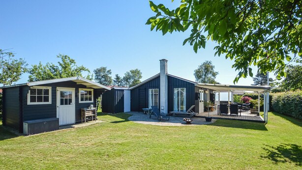 Een woonhuis met twee verdiepingen, een overdekte patio en een kleine tuinhuis.