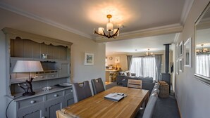 A dining area with a wooden table and chairs, a kitchen with grey cabinets, and a living area with a sofa and curtains. - Delightful highland home in Ballater village (Ballater)