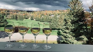 Four wine glasses on a balcony with a view of a golf course and autumn trees.