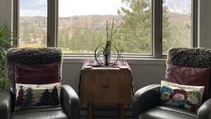 A room with a large window, two leather chairs, a small wooden table, and a potted plant.