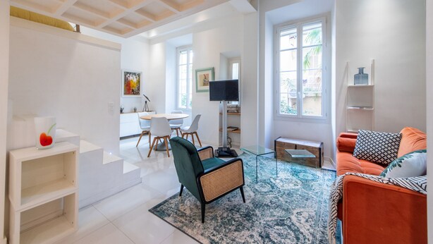 Un salon moderne avec un canapé, un fauteuil, une table basse et un téléviseur. Un escalier mène à une autre pièce.